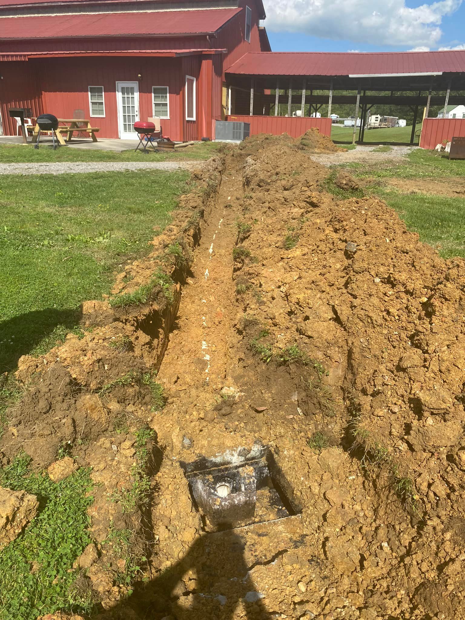 A large pile of dirt is sitting in front of a red barn.