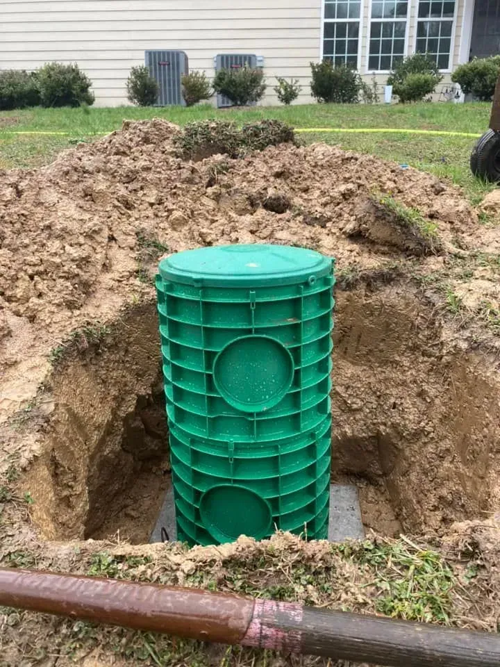 Green utility tank in a dug trench beside a house, with piles of dirt around it.