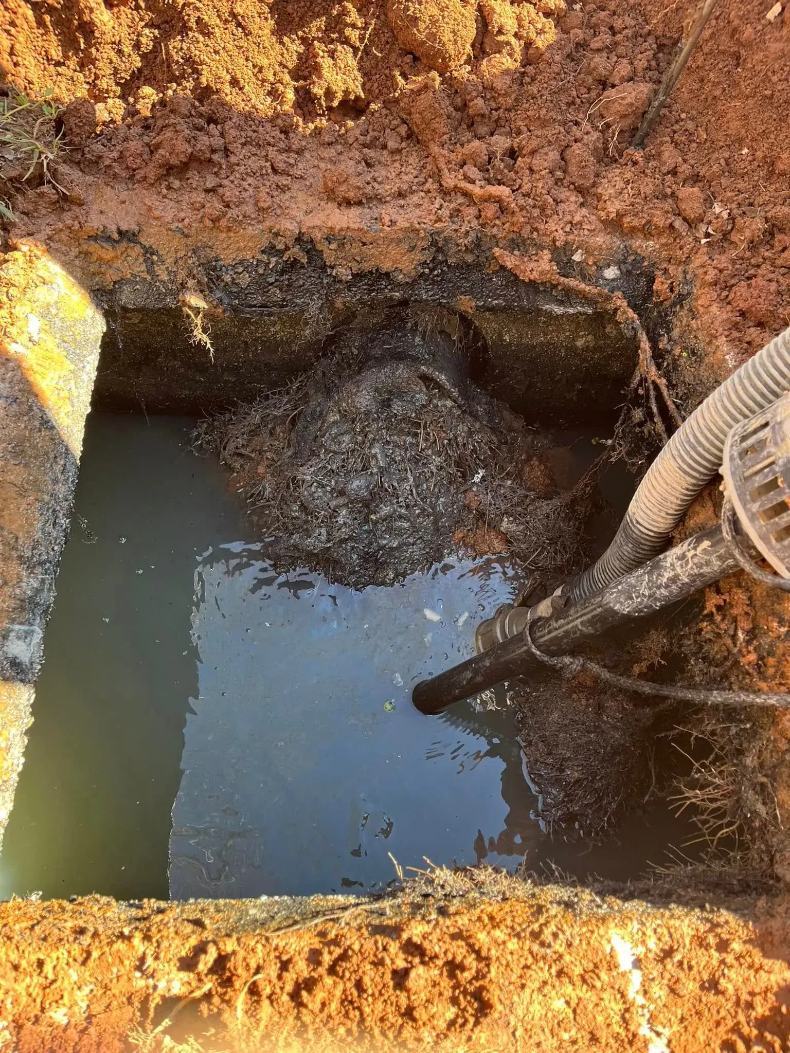 Excavated pit with muddy water and soil walls, a hose pouring water into the trench.
