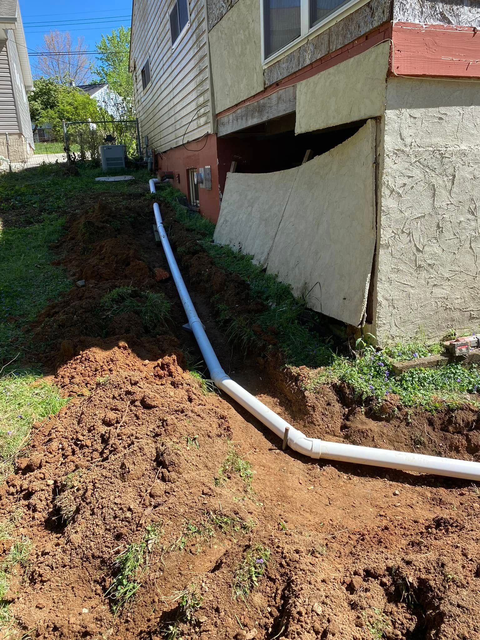 A white pipe is being installed in the dirt next to a house.