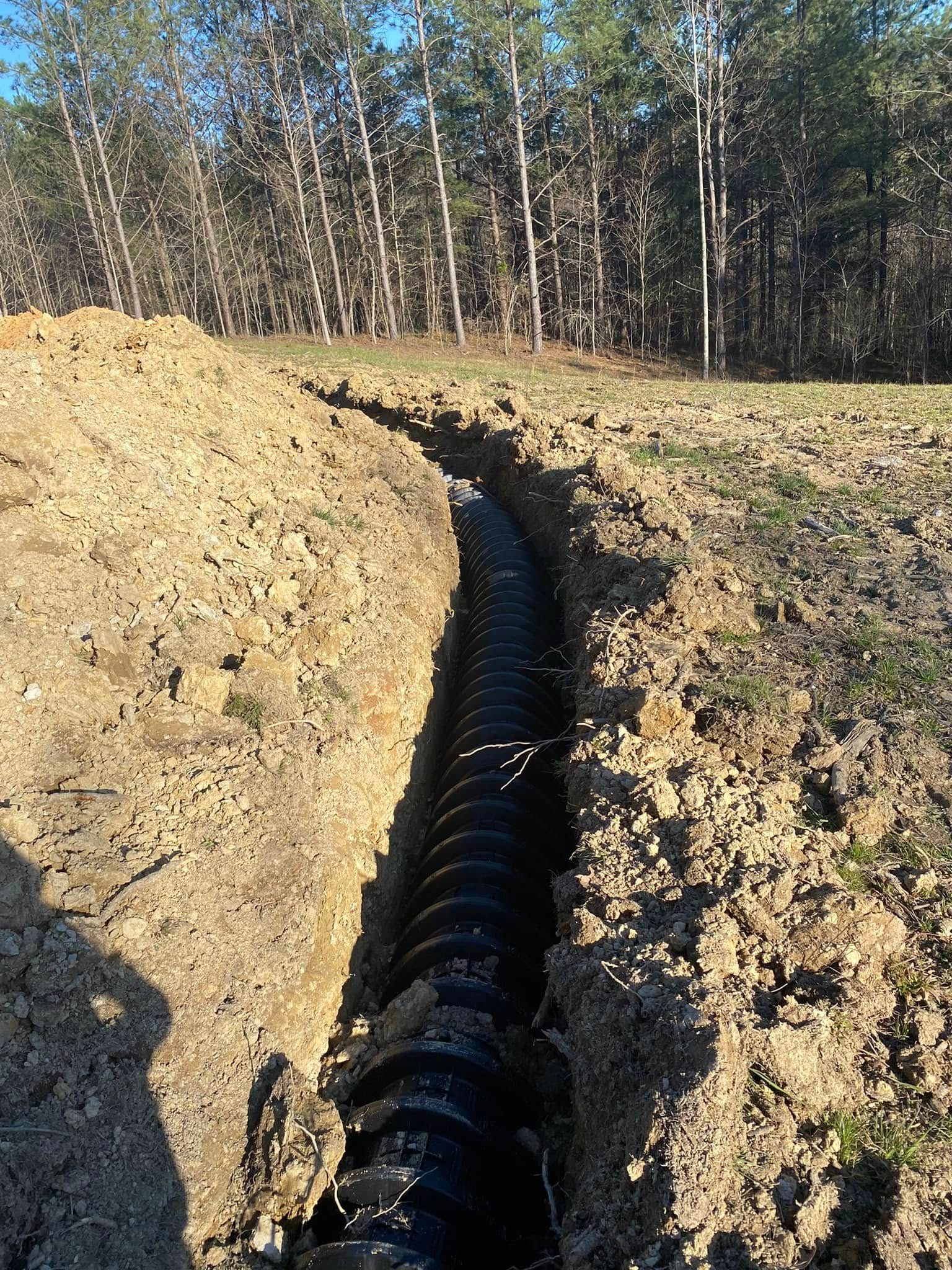 A large black pipe is being installed in a dirt field.