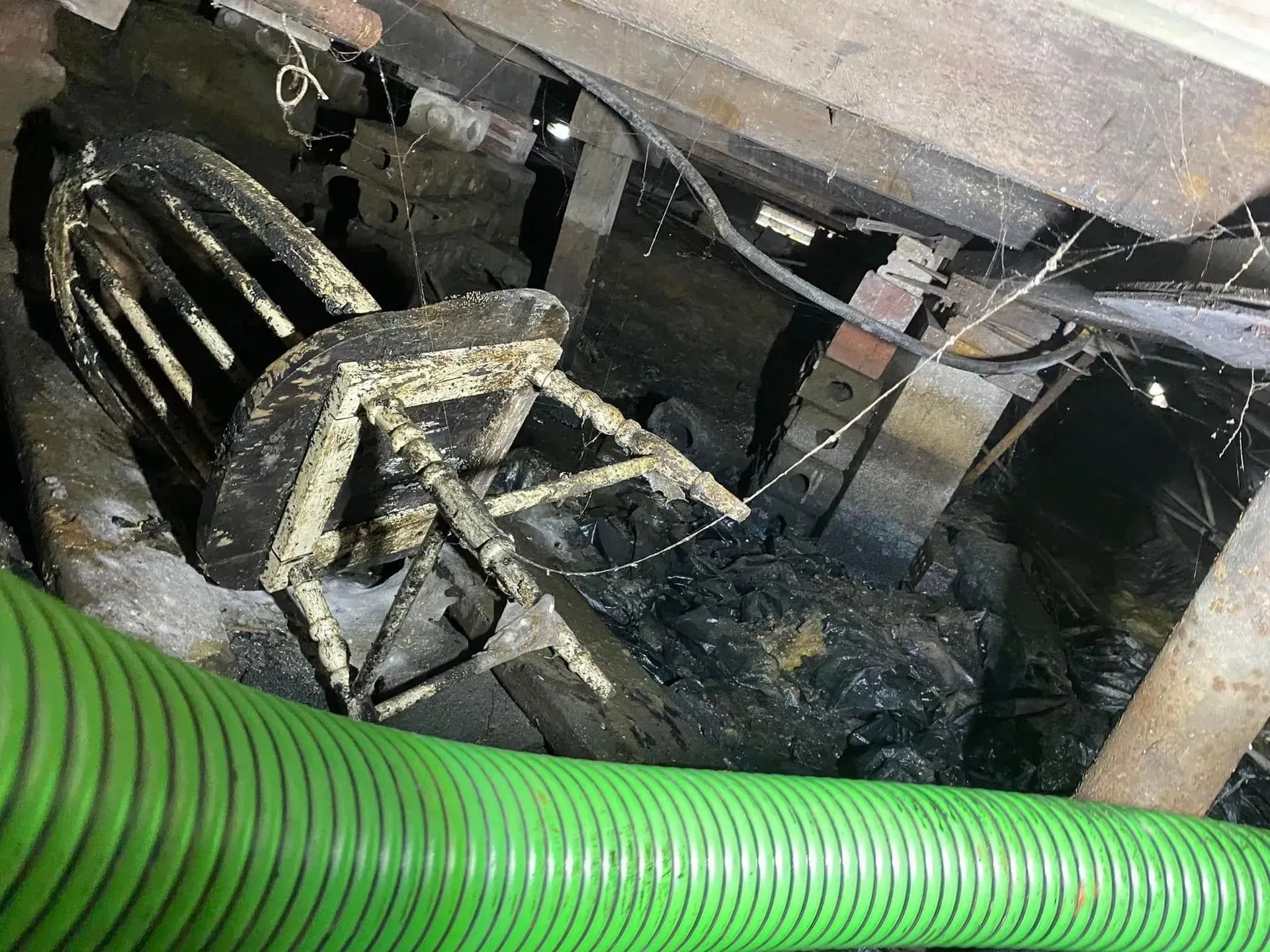 Damaged black chair under a desk with debris and a green hose in the foreground