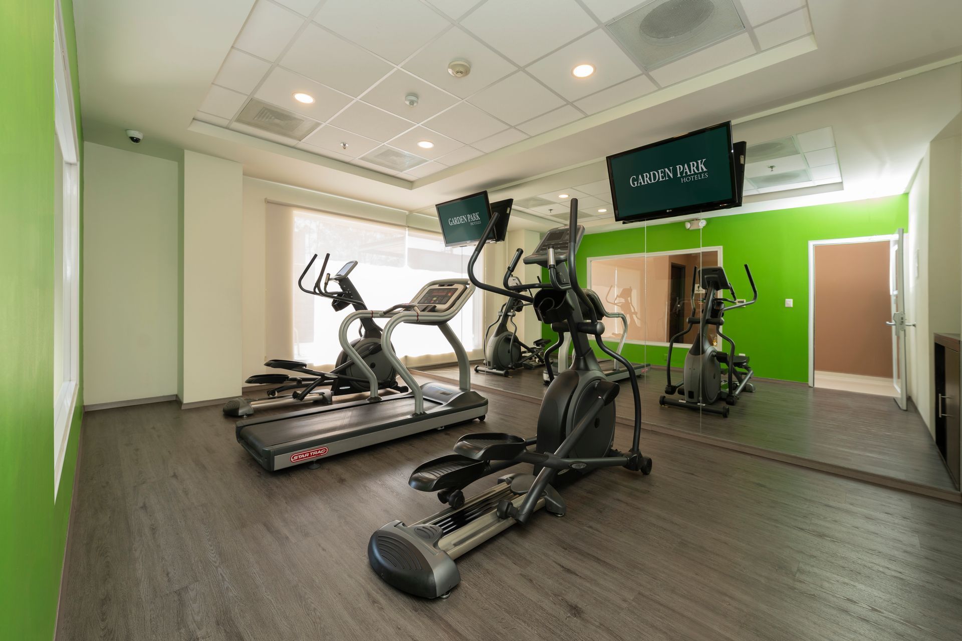 Un gimnasio con cintas de correr, elípticas y un espejo grande.