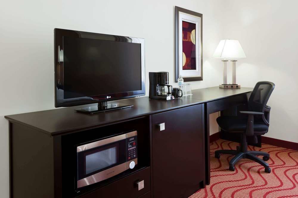 Una habitación de hotel con escritorio, silla, televisión, microondas y cafetera.