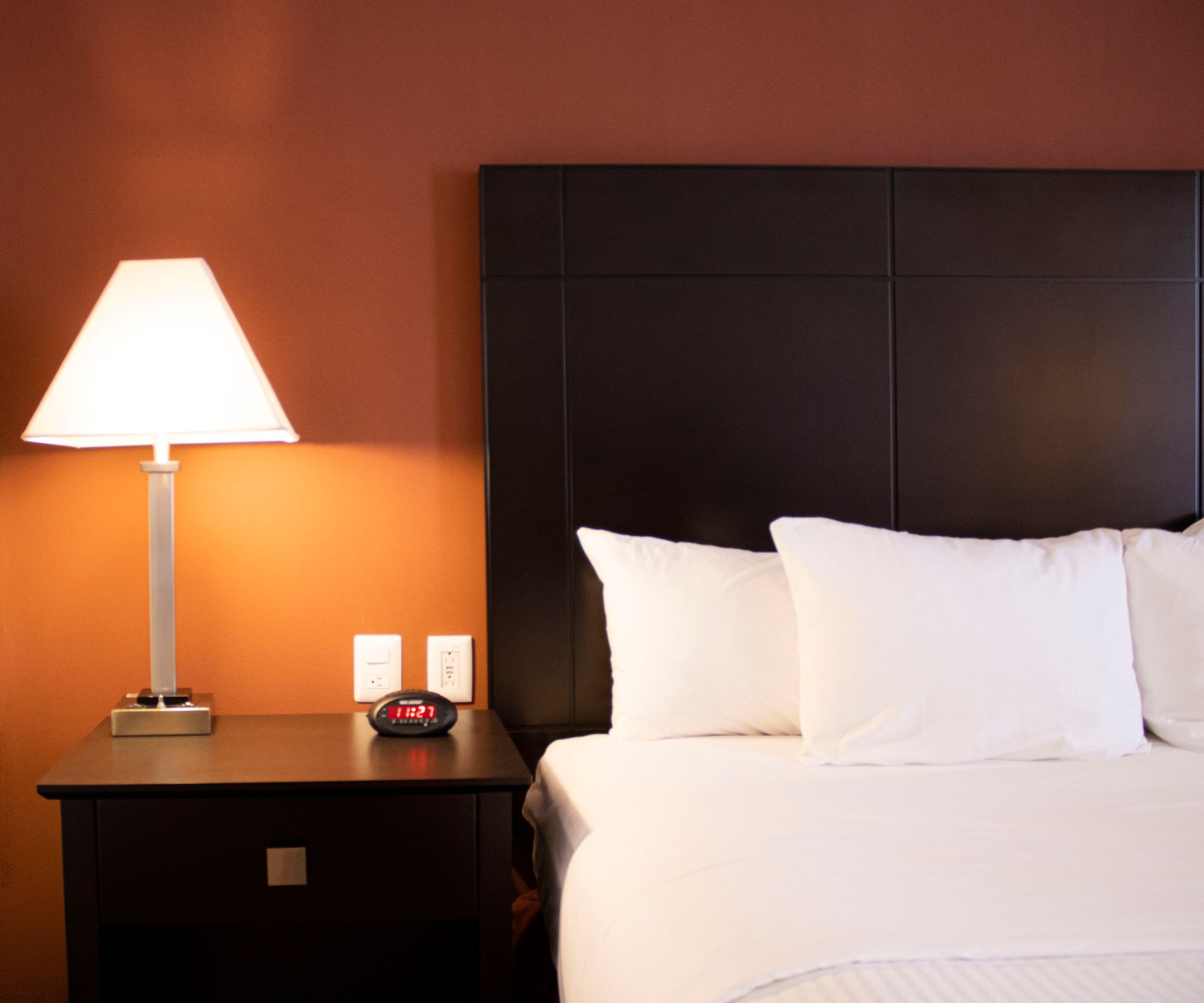 Una habitación de hotel con una cama, una lámpara y un despertador.