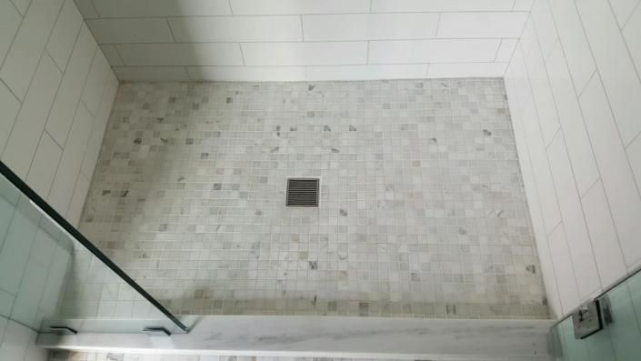 Top-down view of a tiled shower floor with a central drain and glass walls at the bottom edges