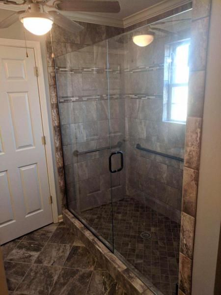 Glass shower enclosure with gray tile and a window in a bathroom