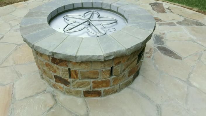 Round stone fire pit with metal grate on a paved patio