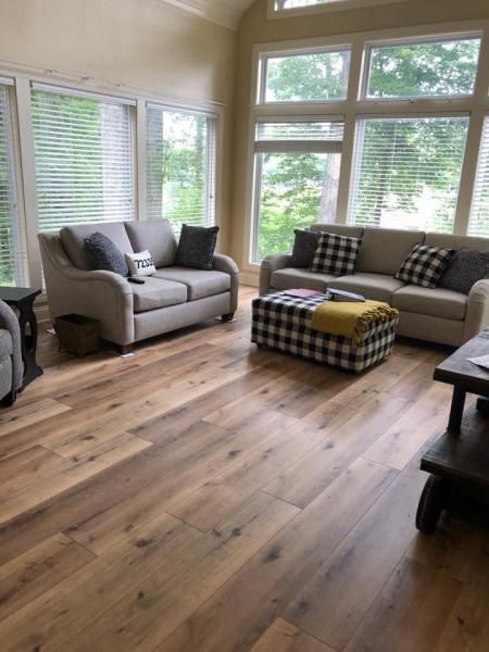 Bright living room with gray sofas, plaid ottoman, and large windows overlooking greenery