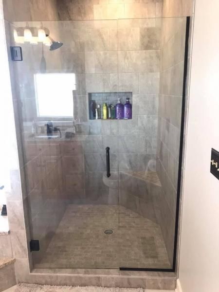Glass walk-in shower with beige tile and built-in shelf of colorful bottles