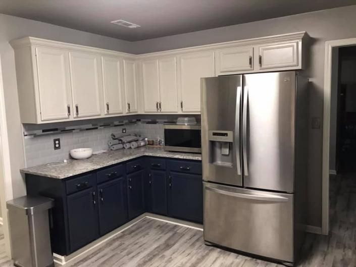 Small kitchen with white and dark blue cabinets, stainless steel refrigerator, and light countertops.