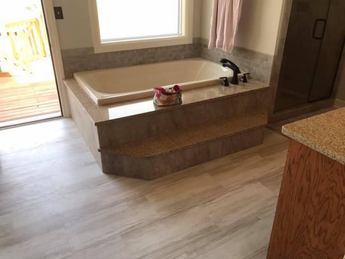 Empty bathroom with a built-in tub, beige tile, wood vanity, and a window opening to a deck.