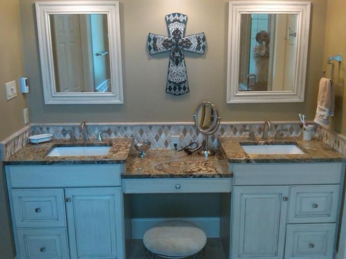 Double vanity bathroom with blue cabinets, granite counters, mirrors, and decorative cross wall art