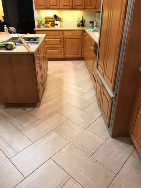 Bright kitchen with wooden cabinets, beige tiled floor, and a central island near a sink.