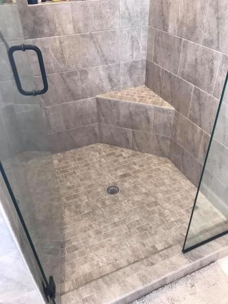 Empty tiled walk-in shower with glass door, gray walls, built-in corner shelf, and floor drain.