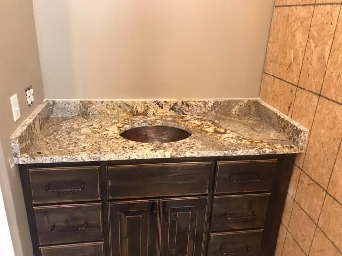 Bathroom vanity with granite countertop, single sink, dark wood cabinets, and tiled walls