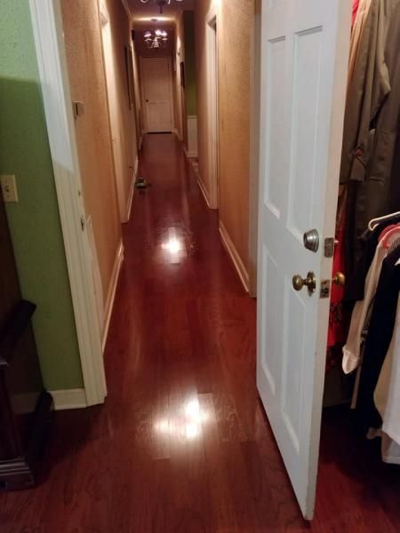 Narrow hallway with glossy wood floors, white doors, and clothes hanging on the right side.