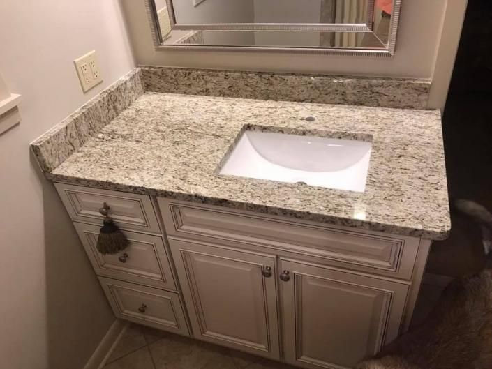 Granite bathroom vanity with white sink, mirrored backsplash, and beige cabinets