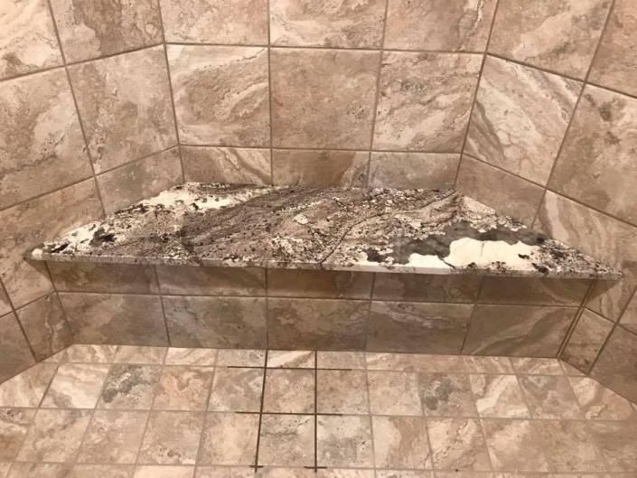 A damaged stone shower bench with chipped tiles and debris in a tiled bathroom