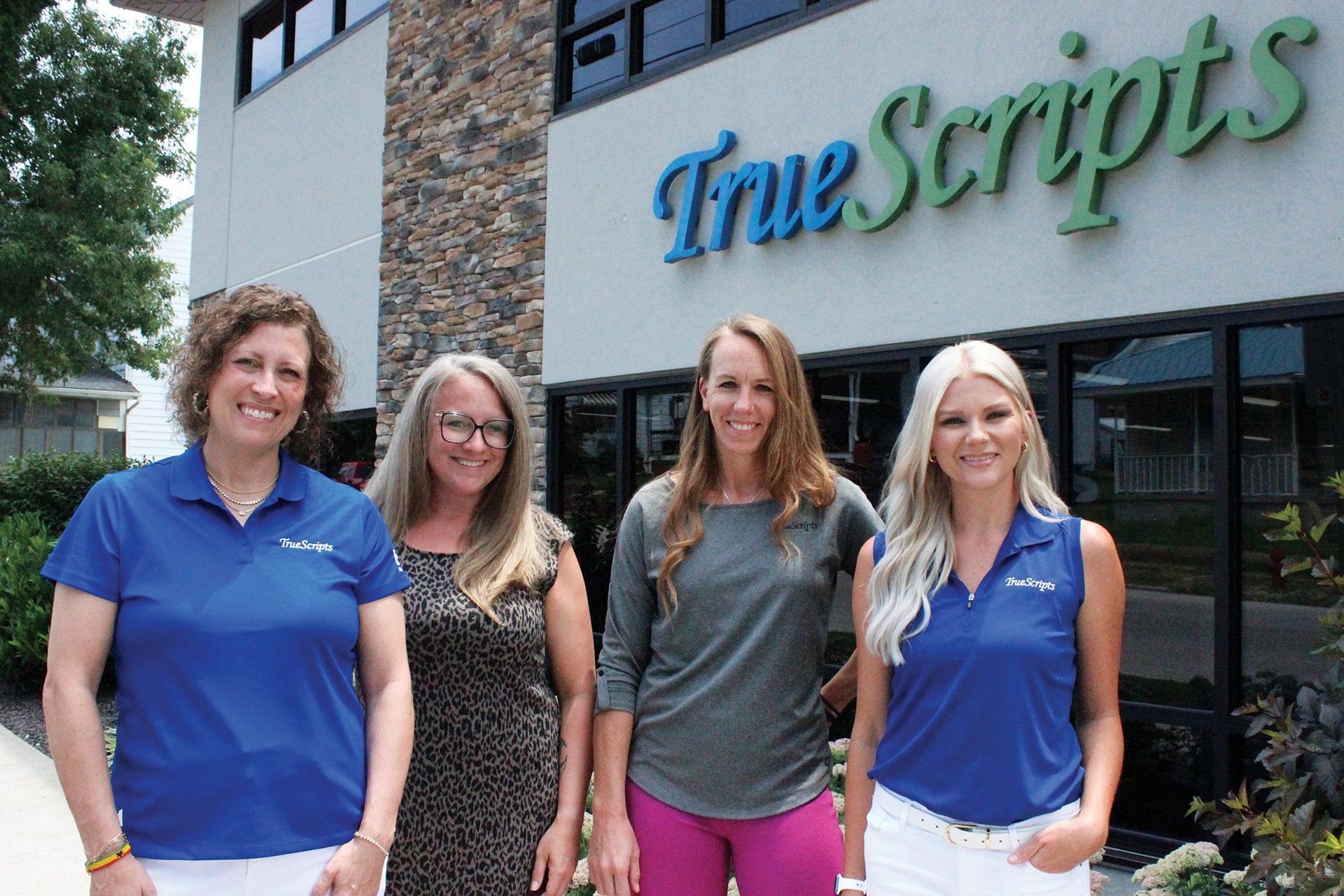 Four female TrueScripts employees posing in front of the office