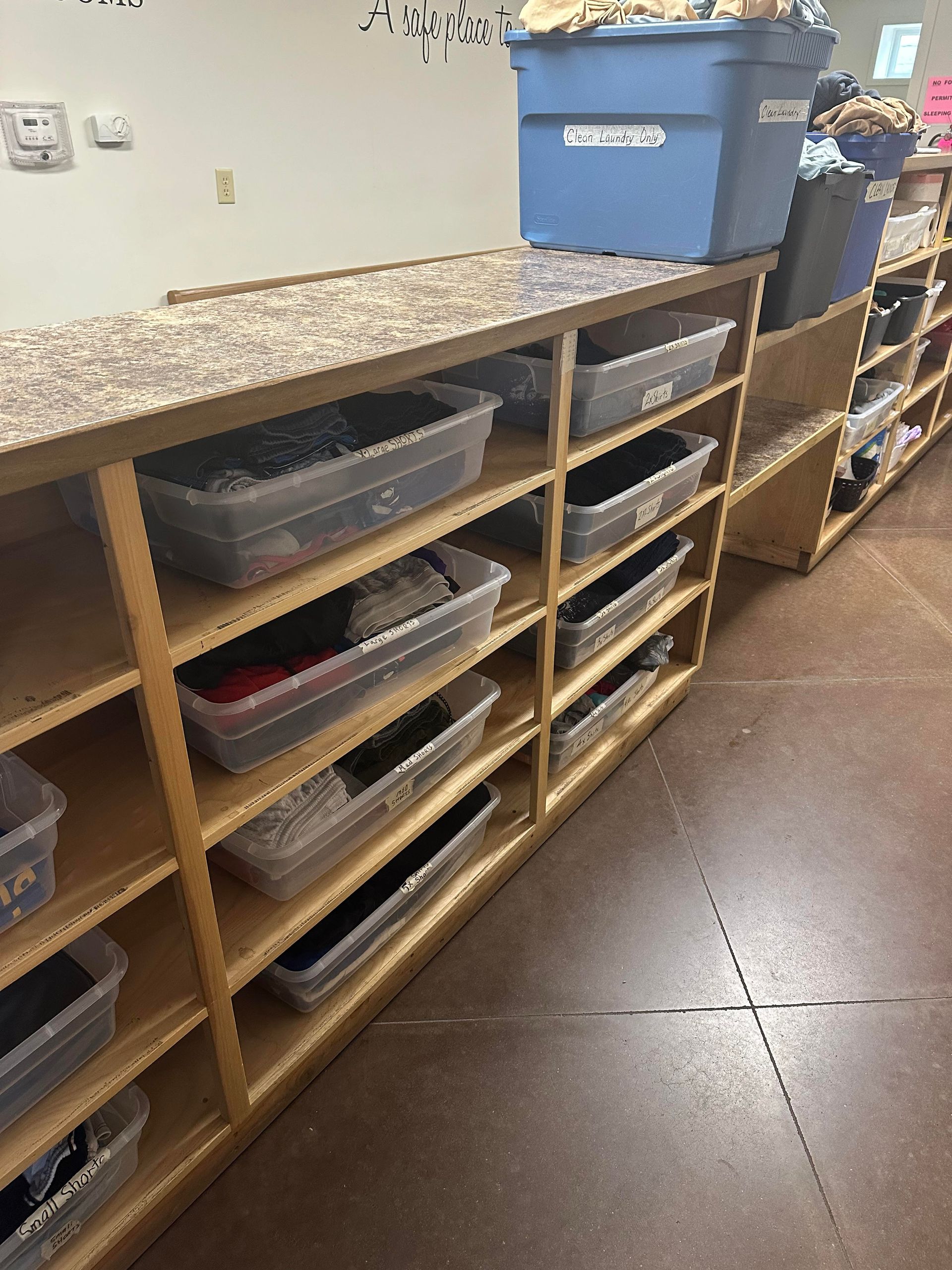 Shelved bins and supplies along a classroom wall beside a countertop and blue storage bin.