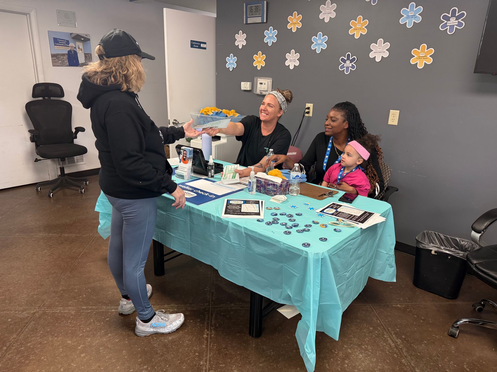 People at a turquoise-covered table at a community event, with crafts and decorations on the wall.