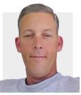 Portrait of a man with short gray hair wearing a light gray shirt against a plain white background