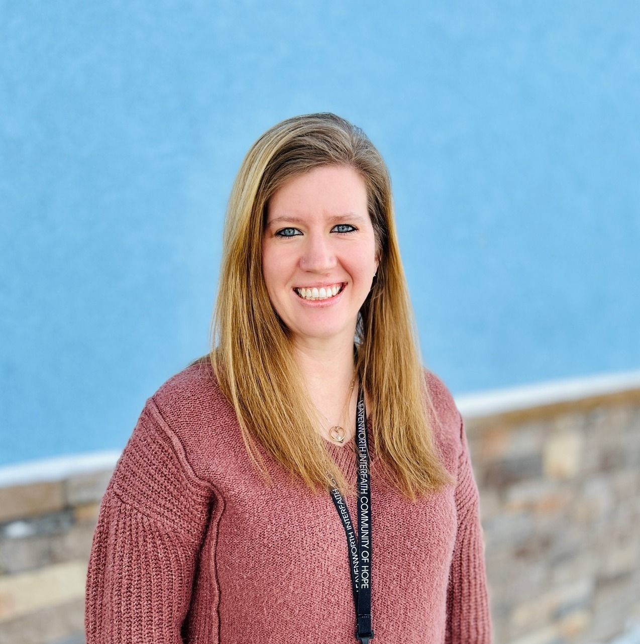 Woman smiling in a maroon sweater against a blue wall and stone ledge