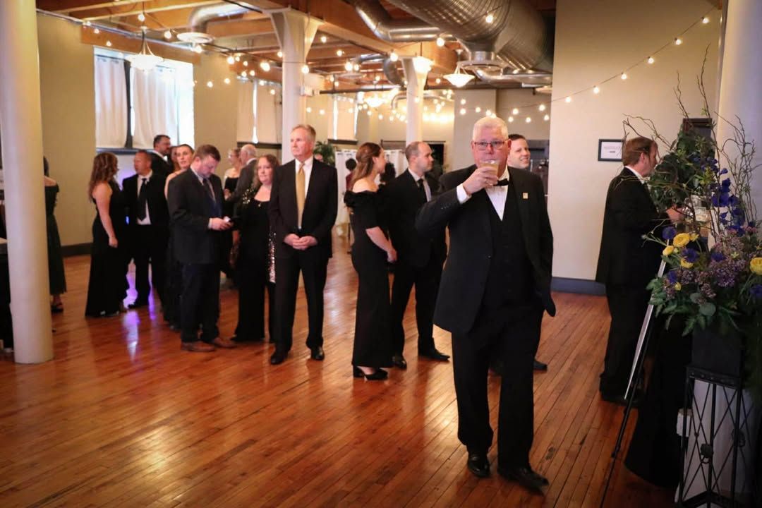 People in formal attire mingling in a warmly lit hall with a polished wooden floor