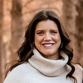 A woman is wearing a white turtleneck sweater and smiling.