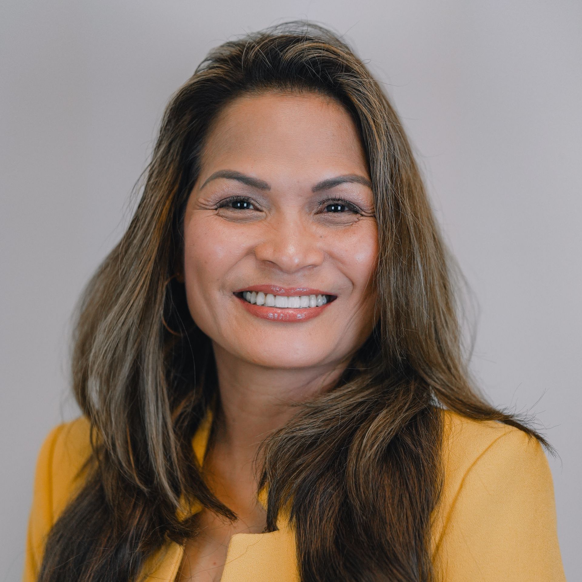 A woman in a yellow jacket is smiling for the camera.