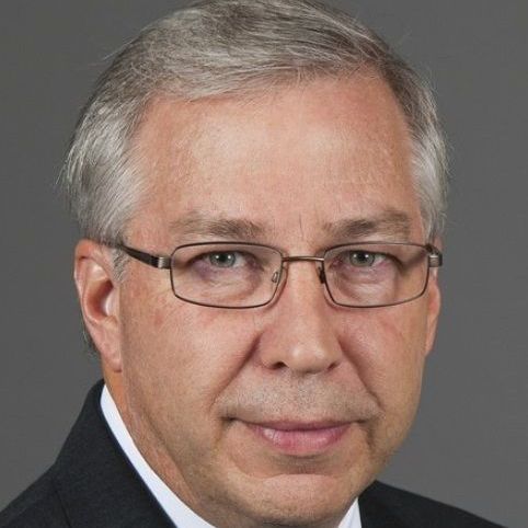 A man wearing glasses and a suit is smiling for the camera.