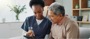 A nurse is showing an elderly man how to use a tablet.