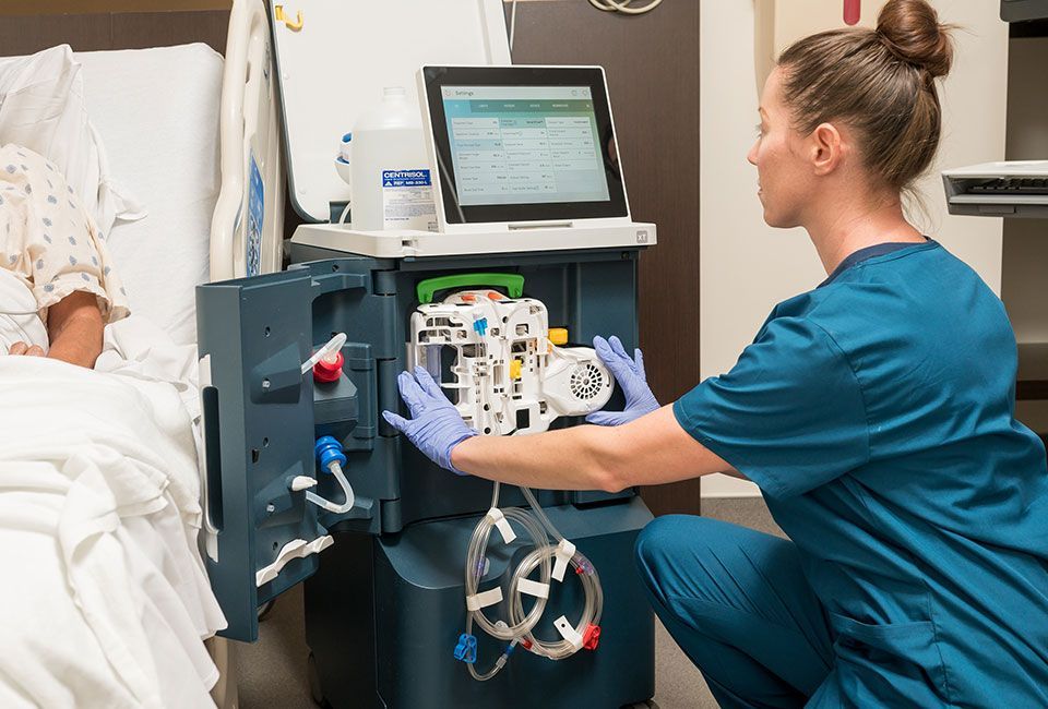 a nurse setting up a dialyzer so patient can start hemodialysis treatment