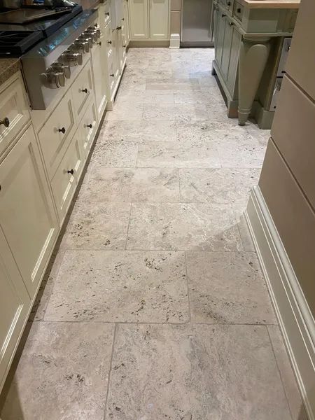 Narrow kitchen with light stone tile floor, white cabinets, and stainless steel appliances.