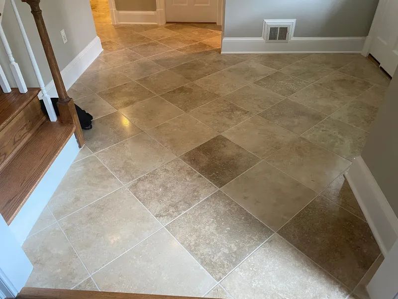 Empty tiled hallway with beige diamond-pattern floor and white baseboards leading to a doorway.