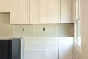 Empty white kitchen cabinets and countertop area with a window on the right.