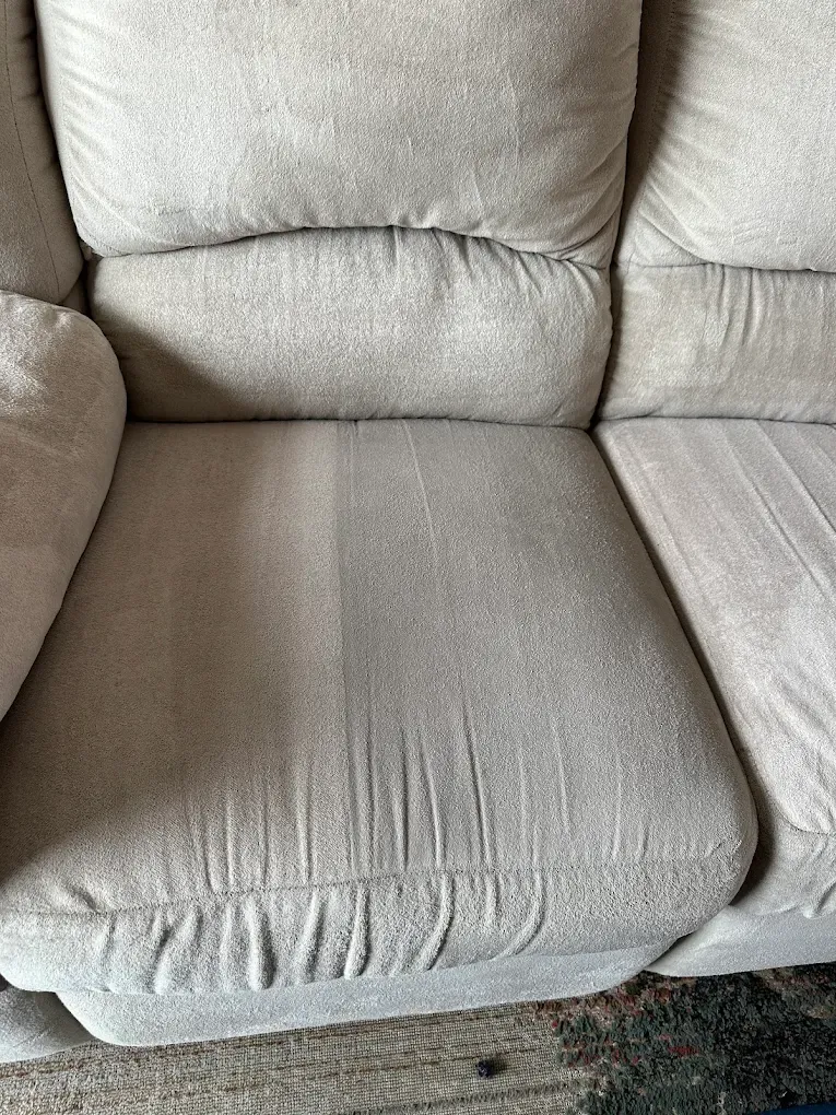 A beige upholstered sofa cushion showing a clear contrast between a cleaned, lighter side and a soiled, darker side.