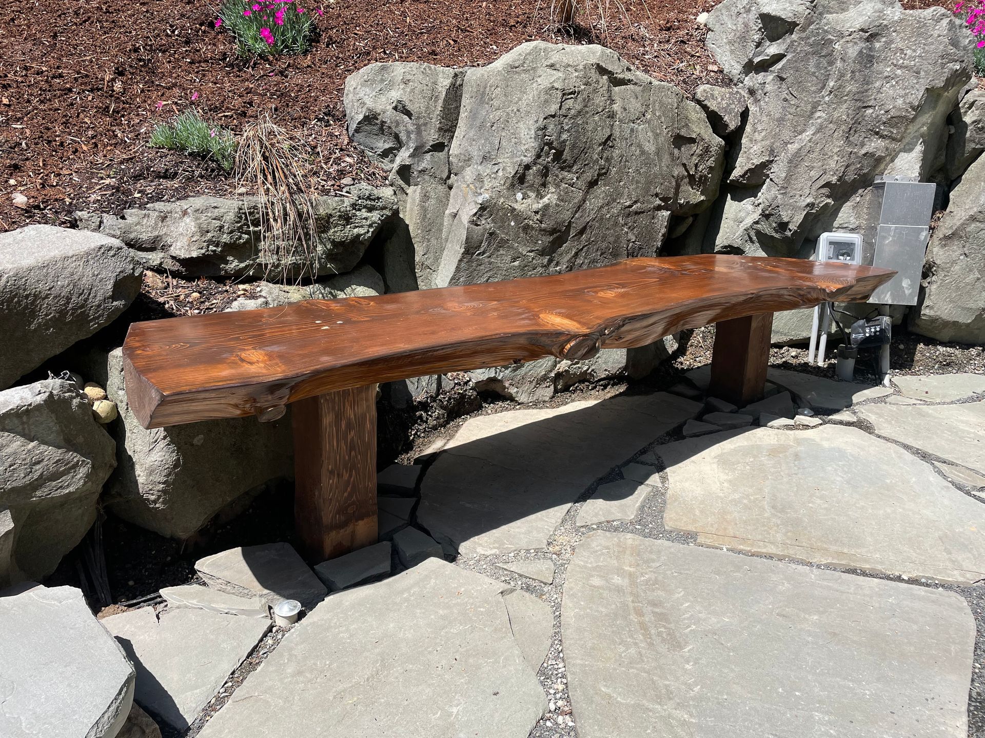 A wooden bench is sitting on a stone walkway next to a rock wall.