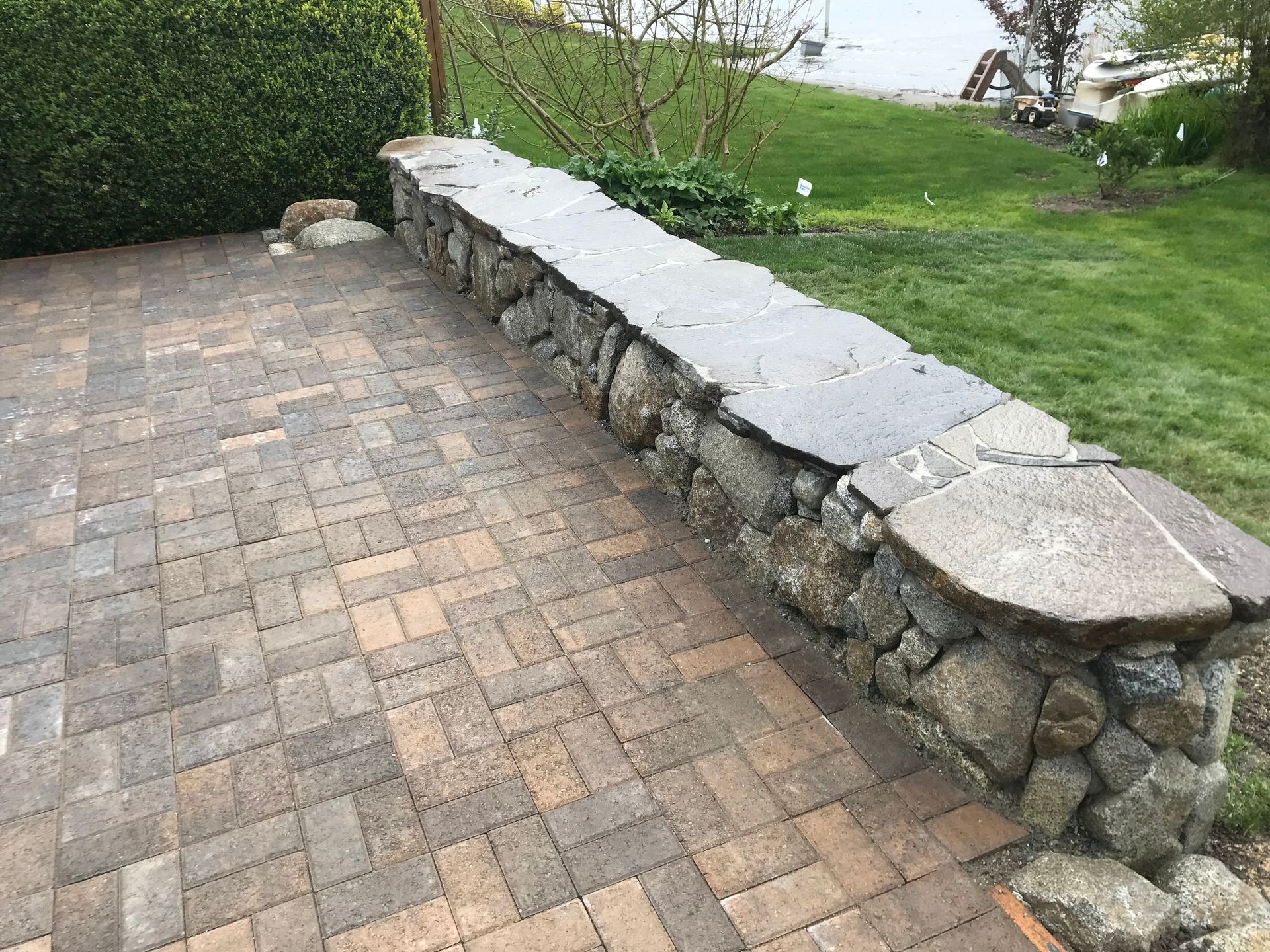 A stone wall surrounds a brick walkway in a yard.