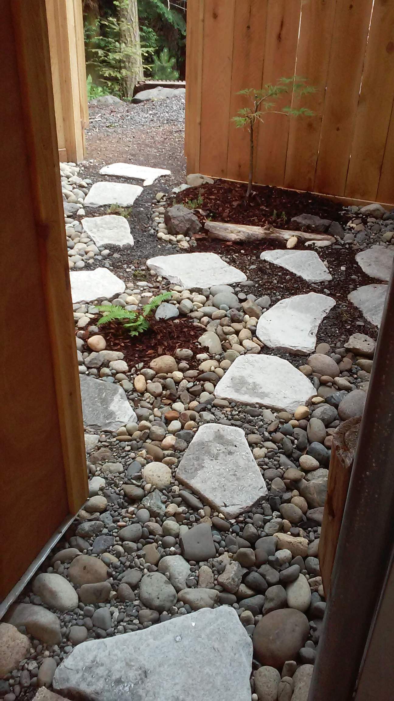A stone walkway leading to a wooden fence surrounded by rocks.