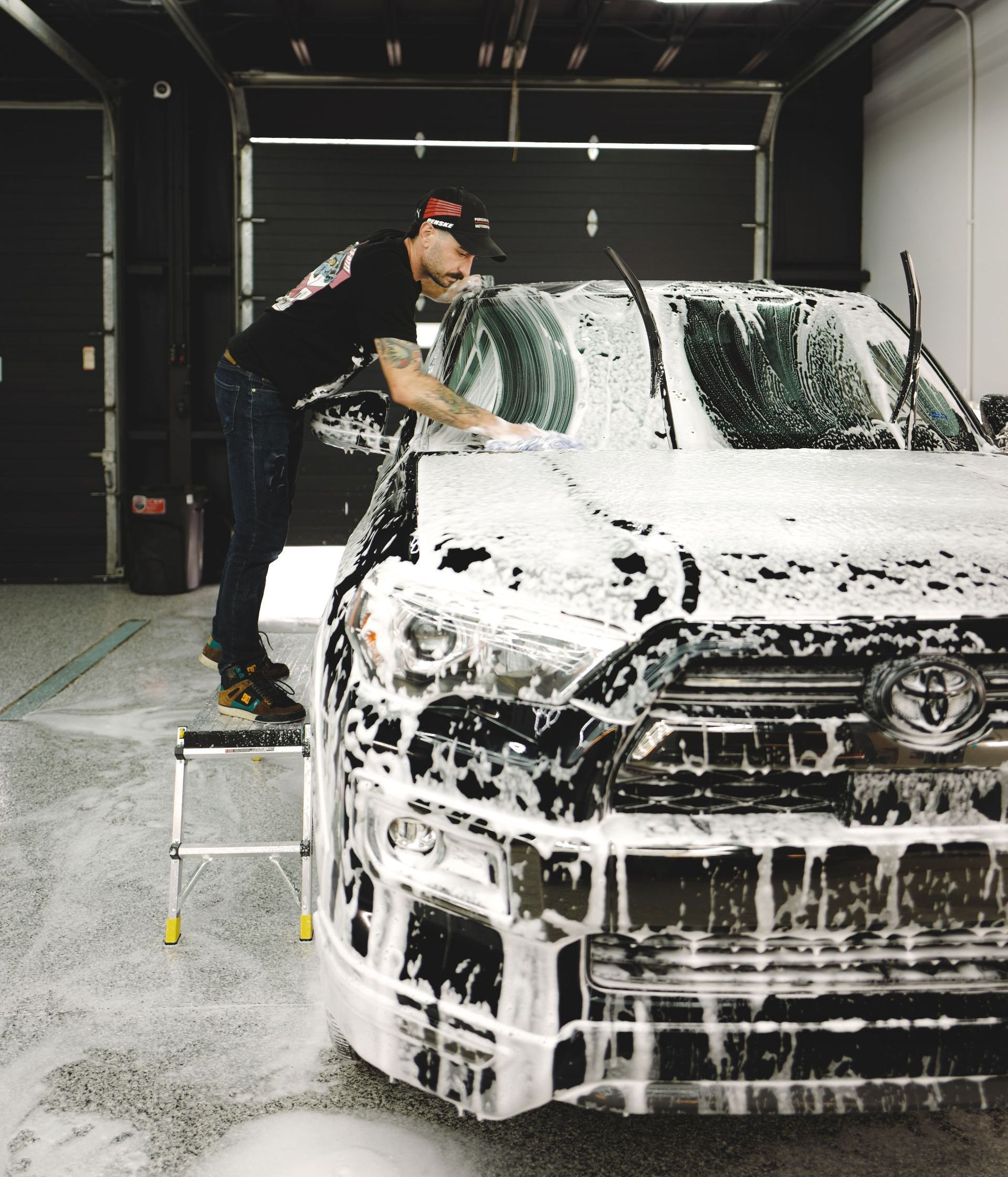 A man is standing on a ladder washing a car