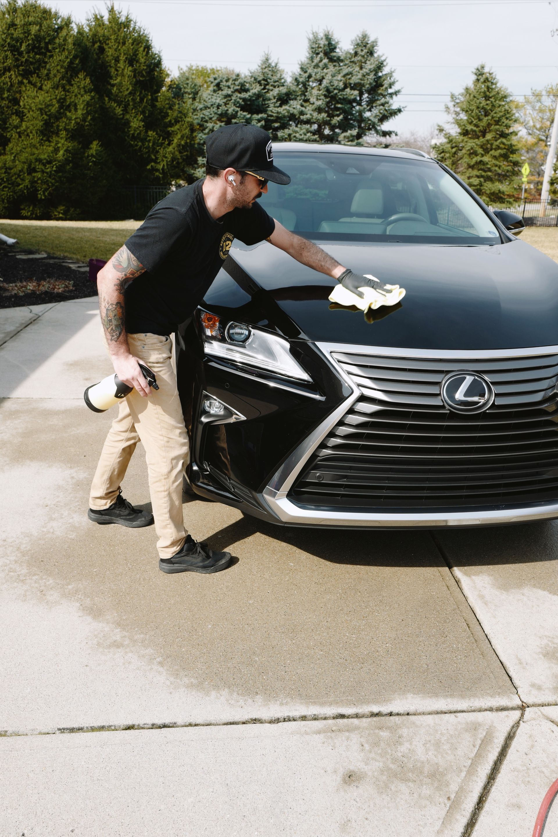 A man is cleaning the hood of a black lexus car.
