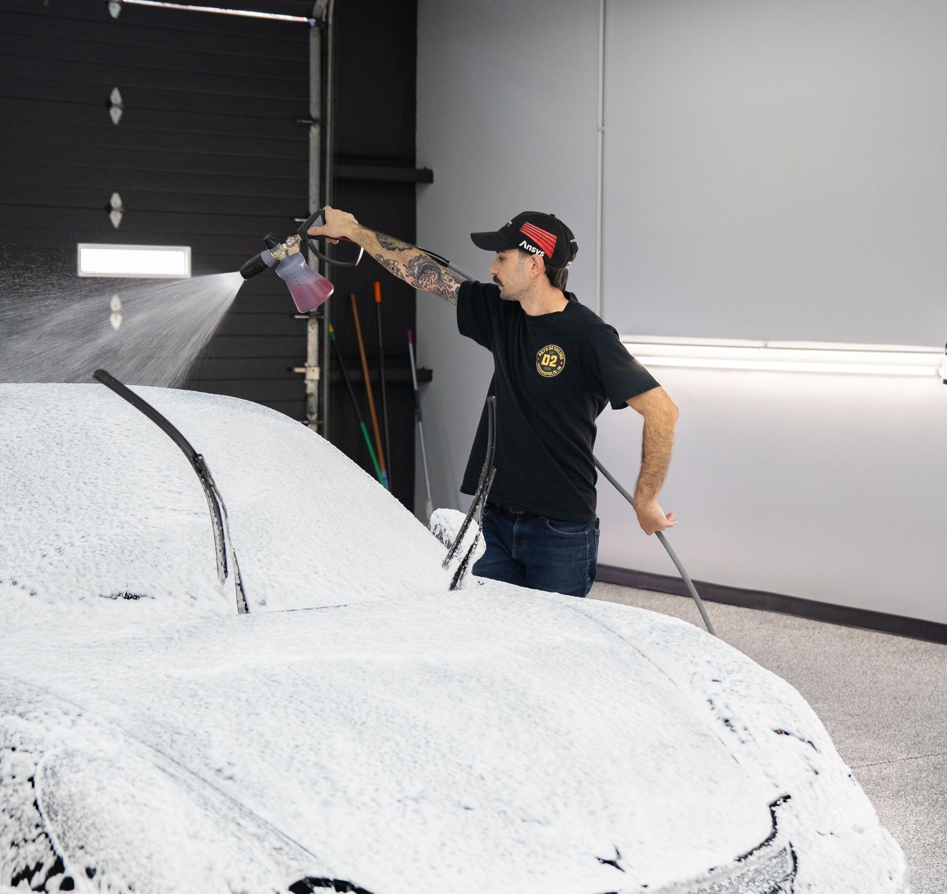 A man is washing a car with foam in a garage.