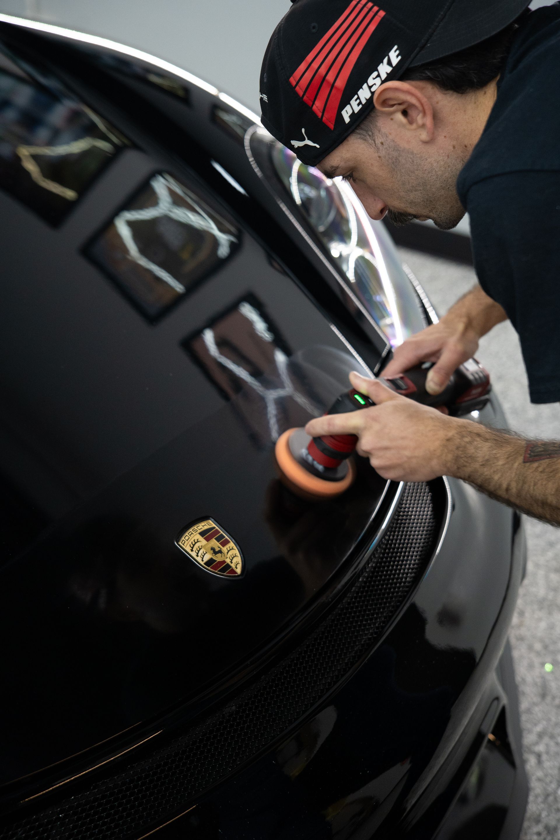 A man is polishing a black car with a polisher.