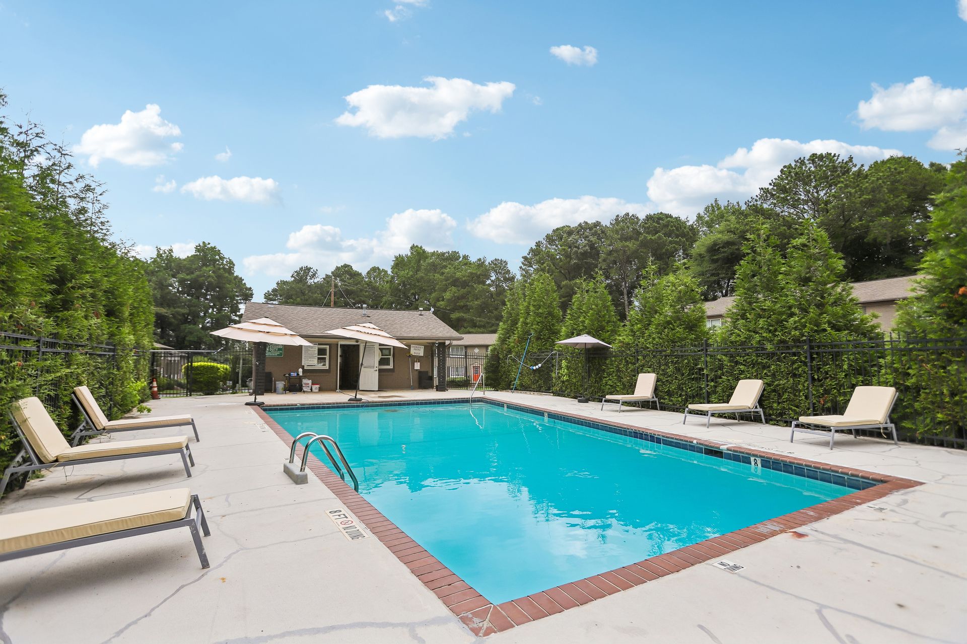 Outdoor swimming pool with lounge chairs and a clubhouse under a blue sky