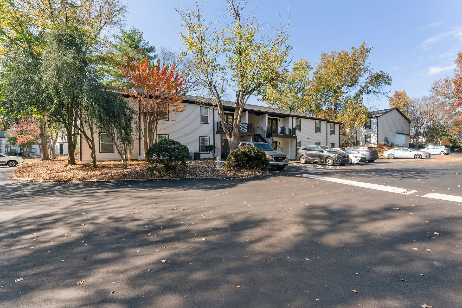Apartment complex parking lot with trees and parked cars in autumn sunlight