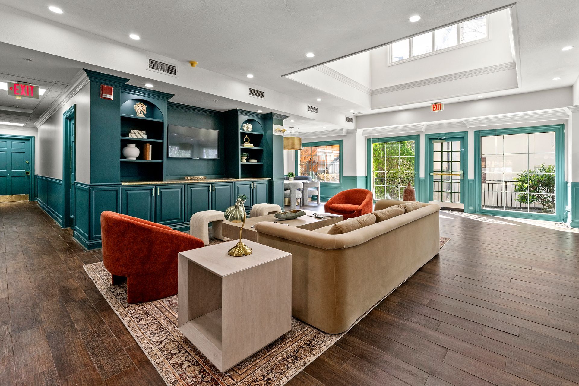 Bright open living room with teal built-ins, beige sofa, red chair, and large windows opening to a patio