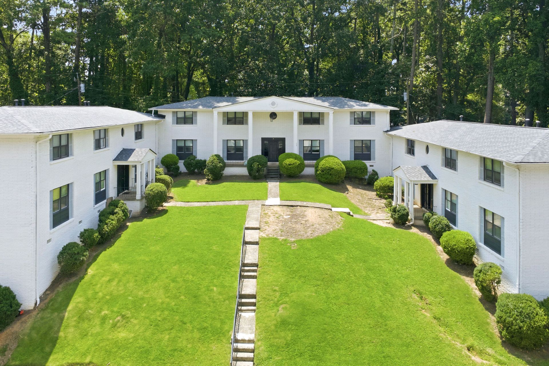 Aerial view of white apartment buildings around a central green courtyard with trees in the background