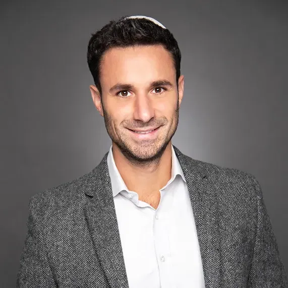 Smiling man in a gray blazer and white shirt against a neutral gray background